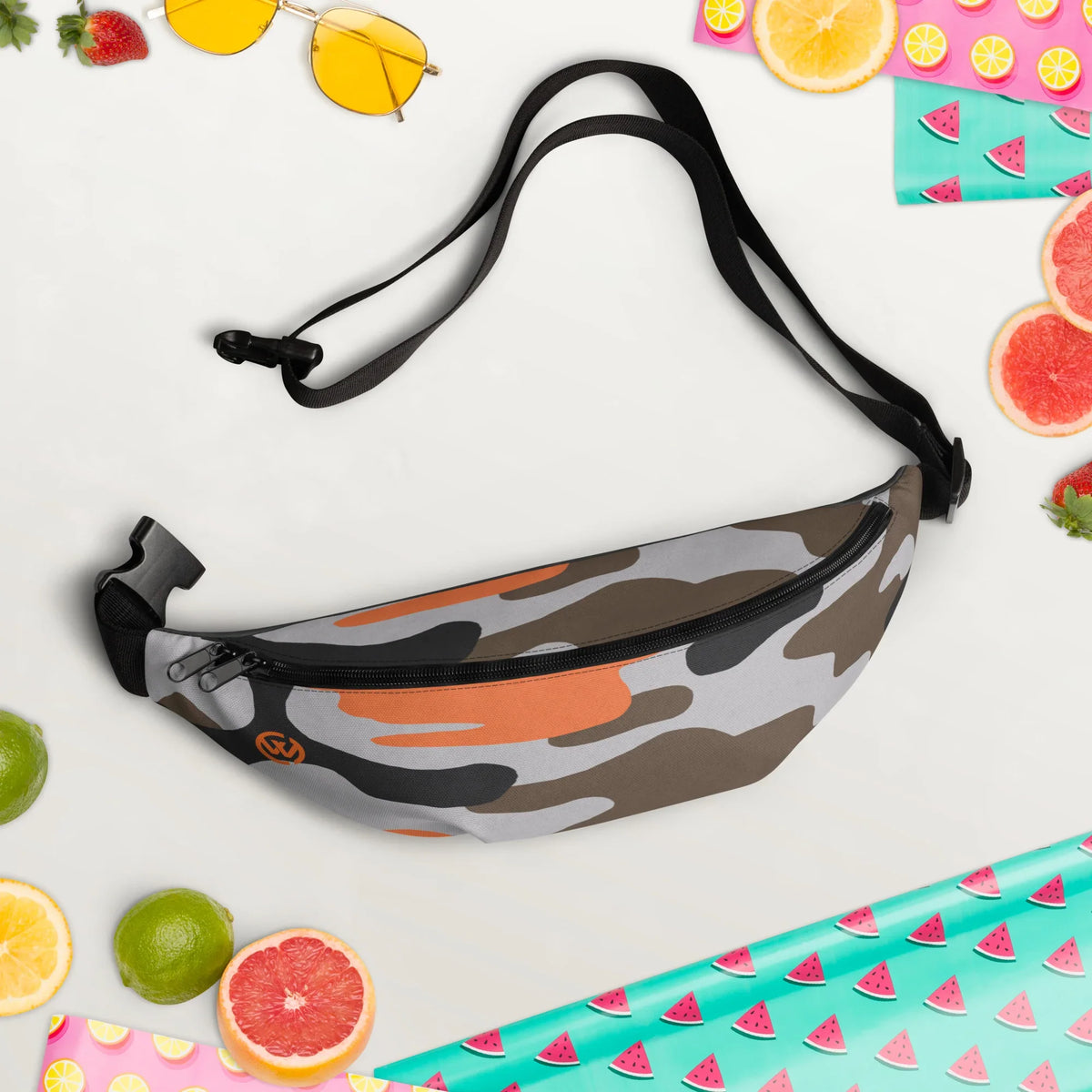 Camouflage-Bauchtasche mit orangefarbenen Akzenten, umgeben von sommerlichen Früchten und Accessoires.