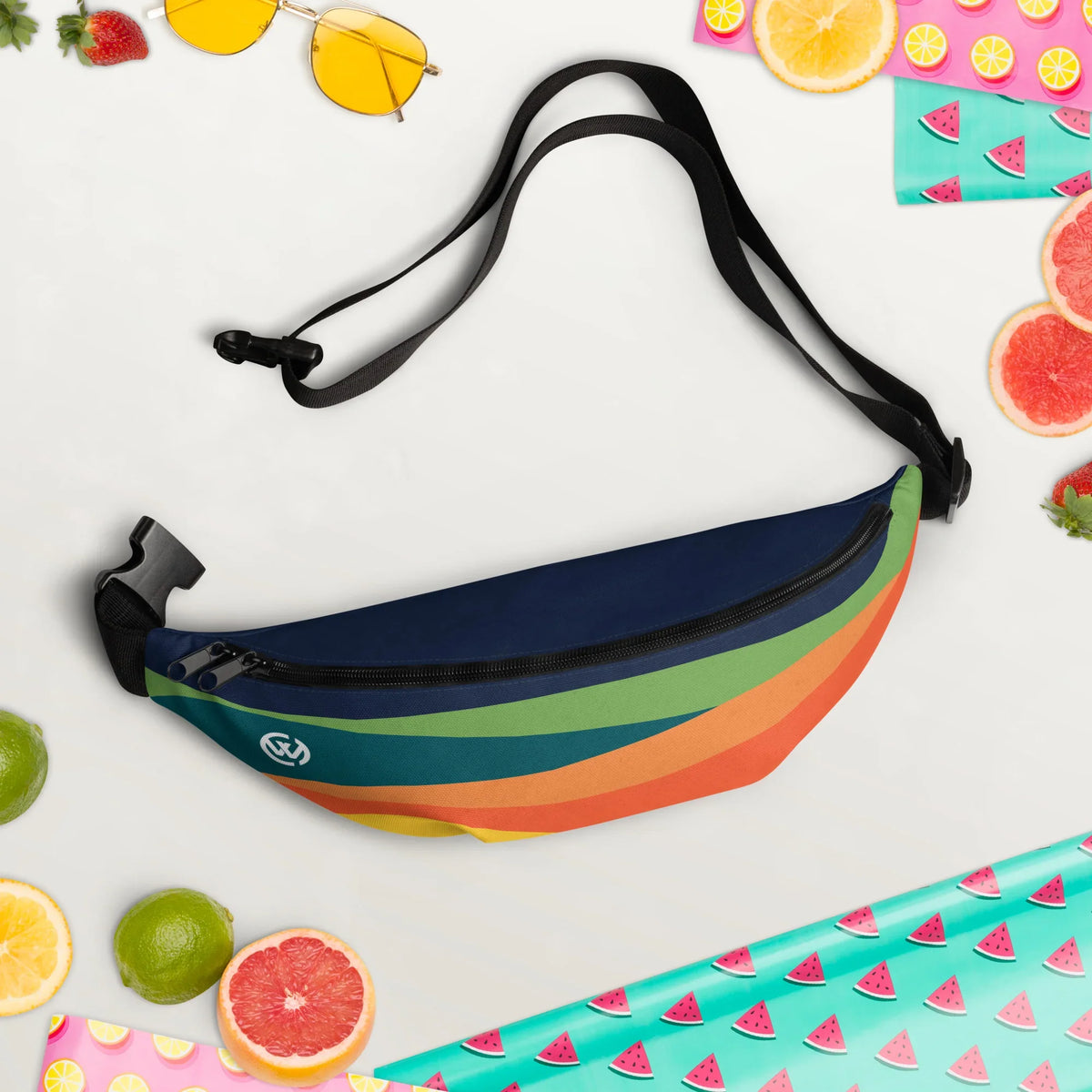 Bunte Bauchtasche mit Regenbogenstreifen, umgeben von sommerlichen Früchten und Accessoires