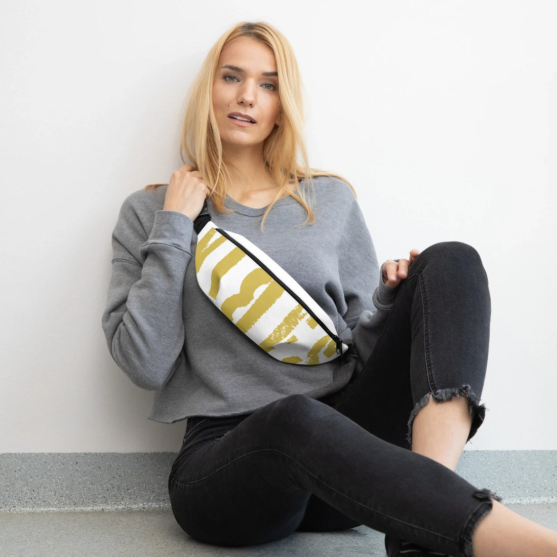 Frau in grauem Sweatshirt und schwarzen Jeans mit gelb-weiß gemusterter Bauchtasche
