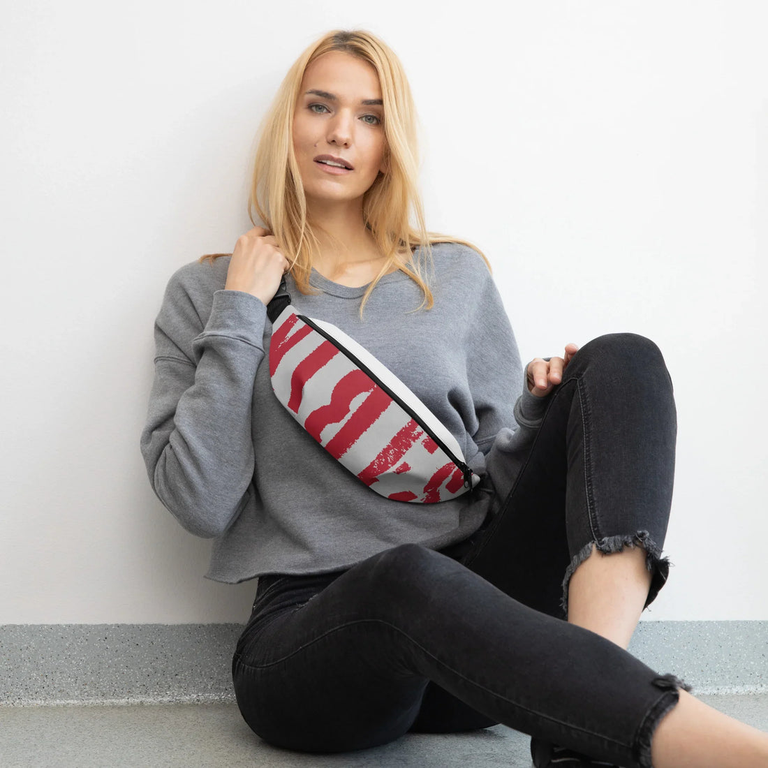 Frau in grauem Sweatshirt und schwarzen Jeans mit einer weiß-roten Bauchtasche