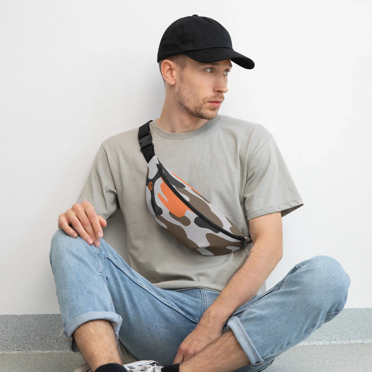 Mann mit grauer T-Shirt, Jeans und einer gemusterten Bauchtasche in Camouflage-Optik.