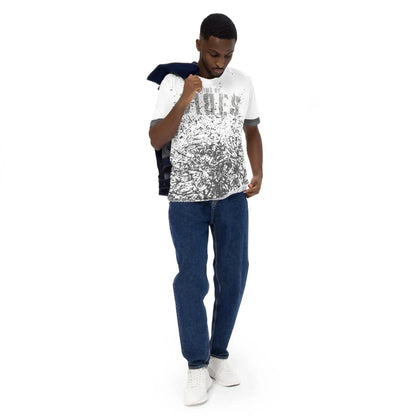Mann trägt weißes Allover-Print T-Shirt, blaue Jeans und weiße Sneaker vor weißem Hintergrund.