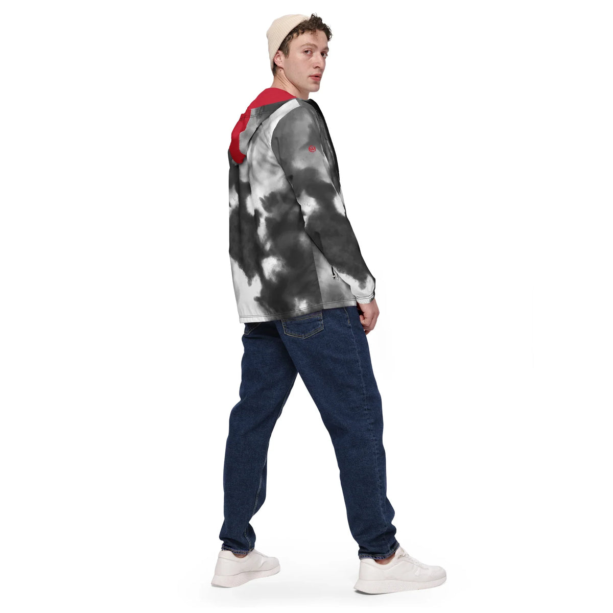 Mann trägt eine schwarz-weiß gemusterte Jacke, blaue Jeans und weiße Sneaker vor weißem Hintergrund.