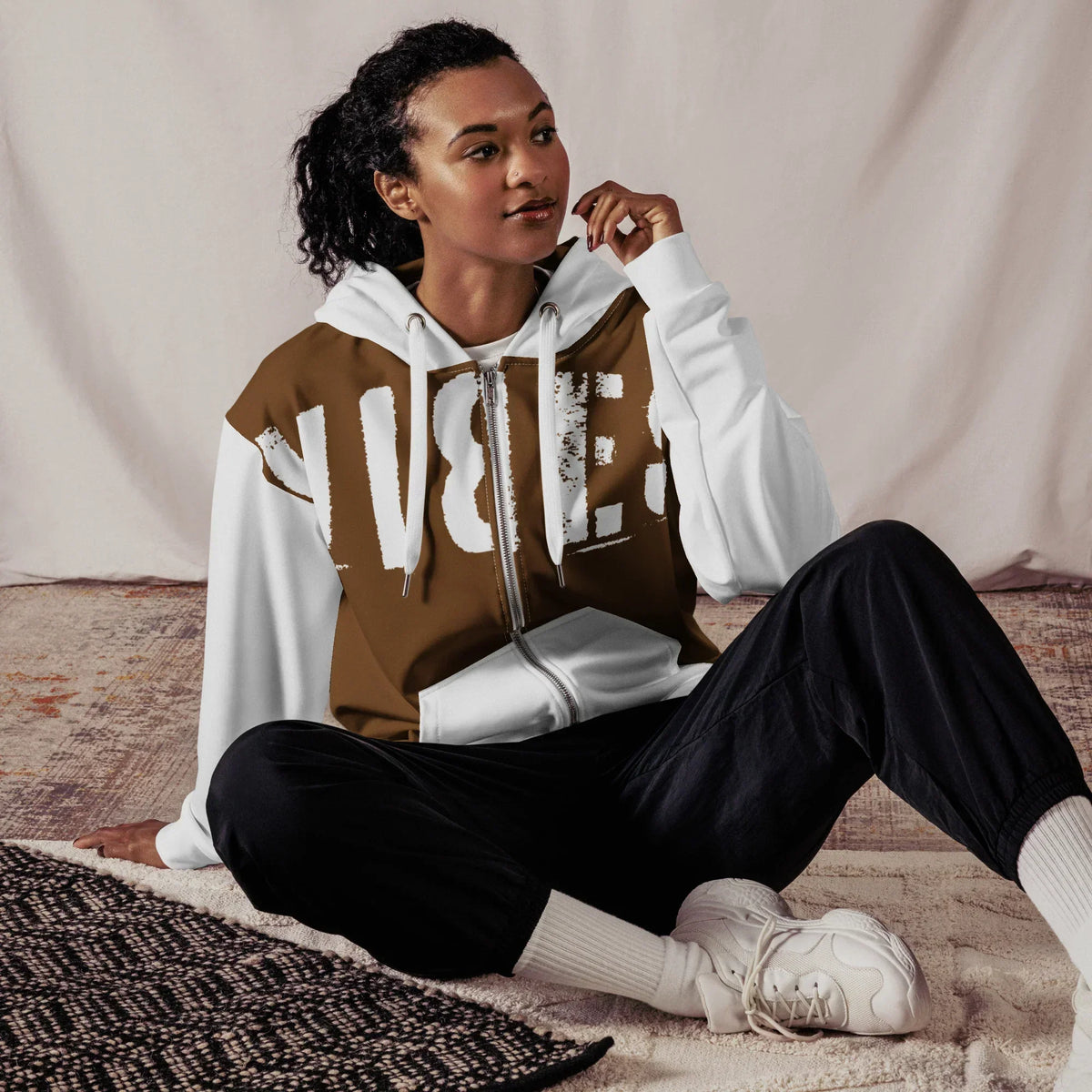 Frau trägt den CREWILD Zip-Hoodie VIBES 2 in Braun und Weiß mit schwarzen Hosen.