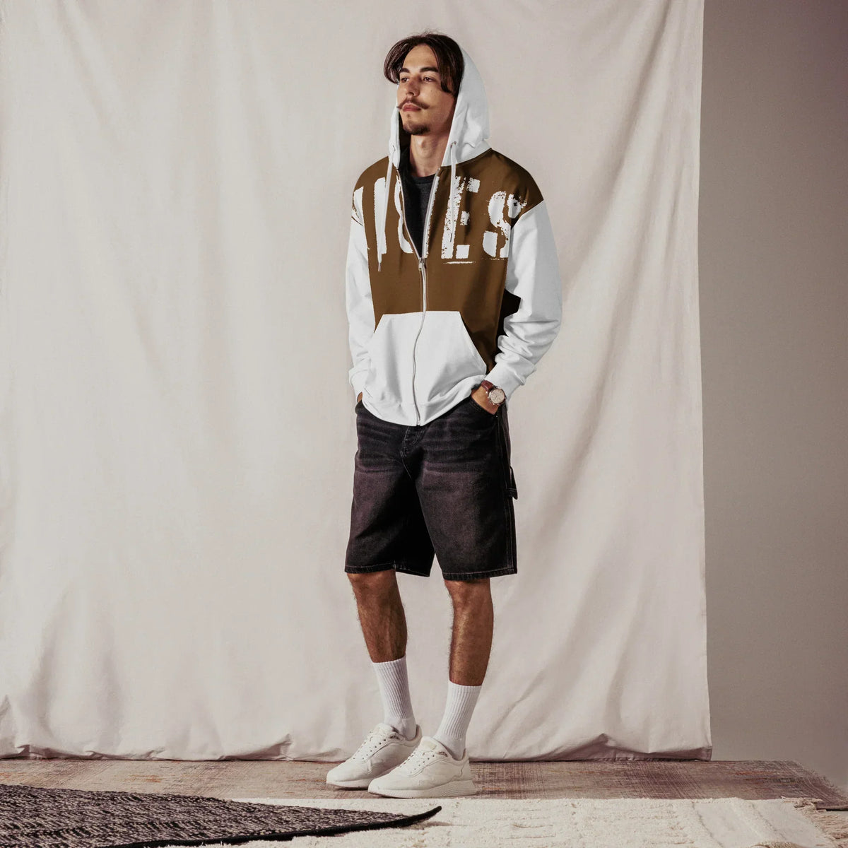 Mann trägt einen braun-weißen CREWILD Zip-Hoodie mit VIBES-Print und dunkle Shorts.