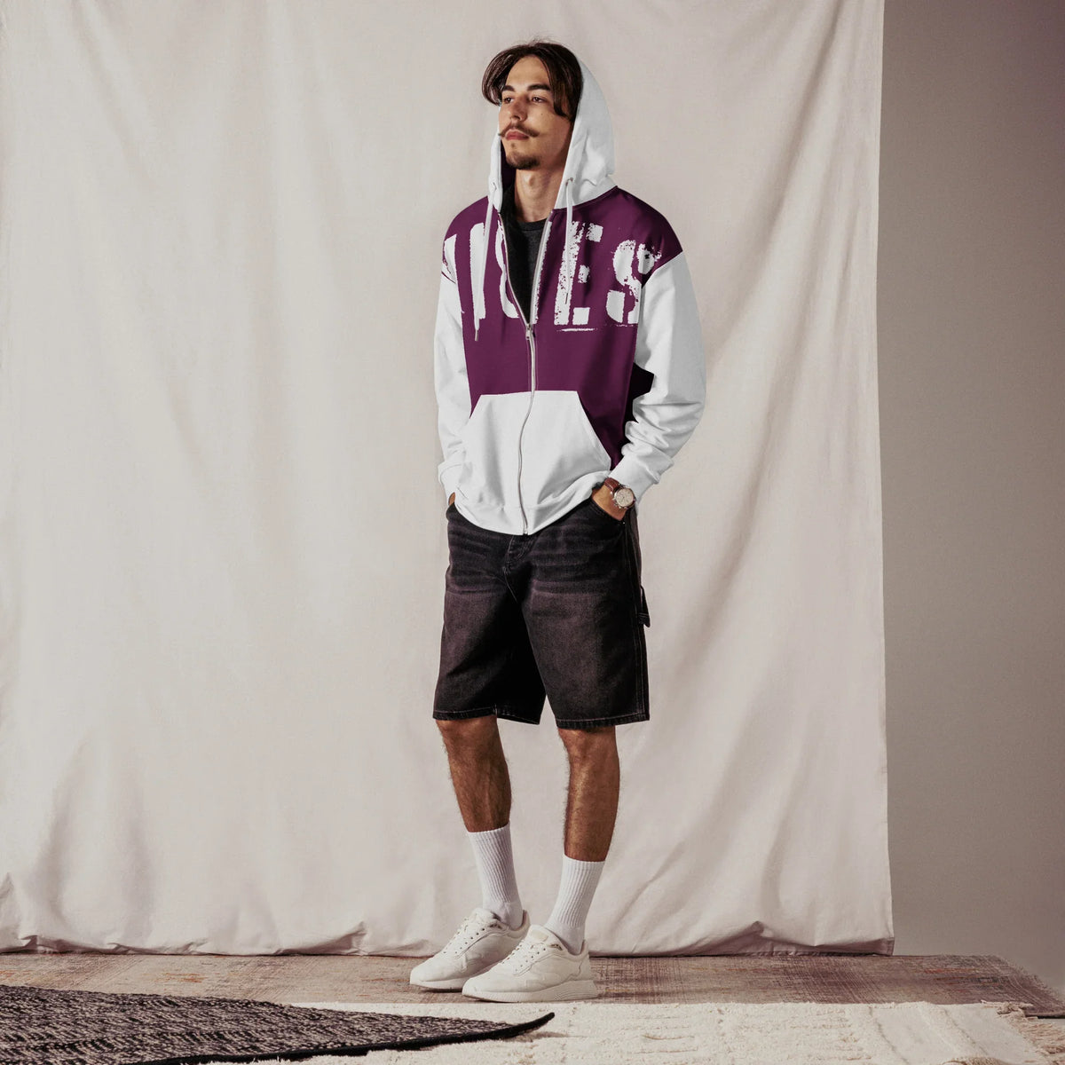 Junger Mann trägt einen zweifarbigen Hoodie mit Grafikprint und Shorts.