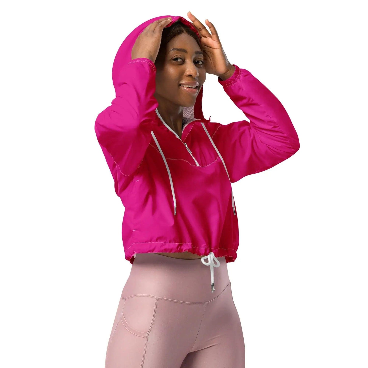 Frau trägt pinken Cropped Windbreaker mit Kapuze und hellrosa Leggings, weißer Hintergrund