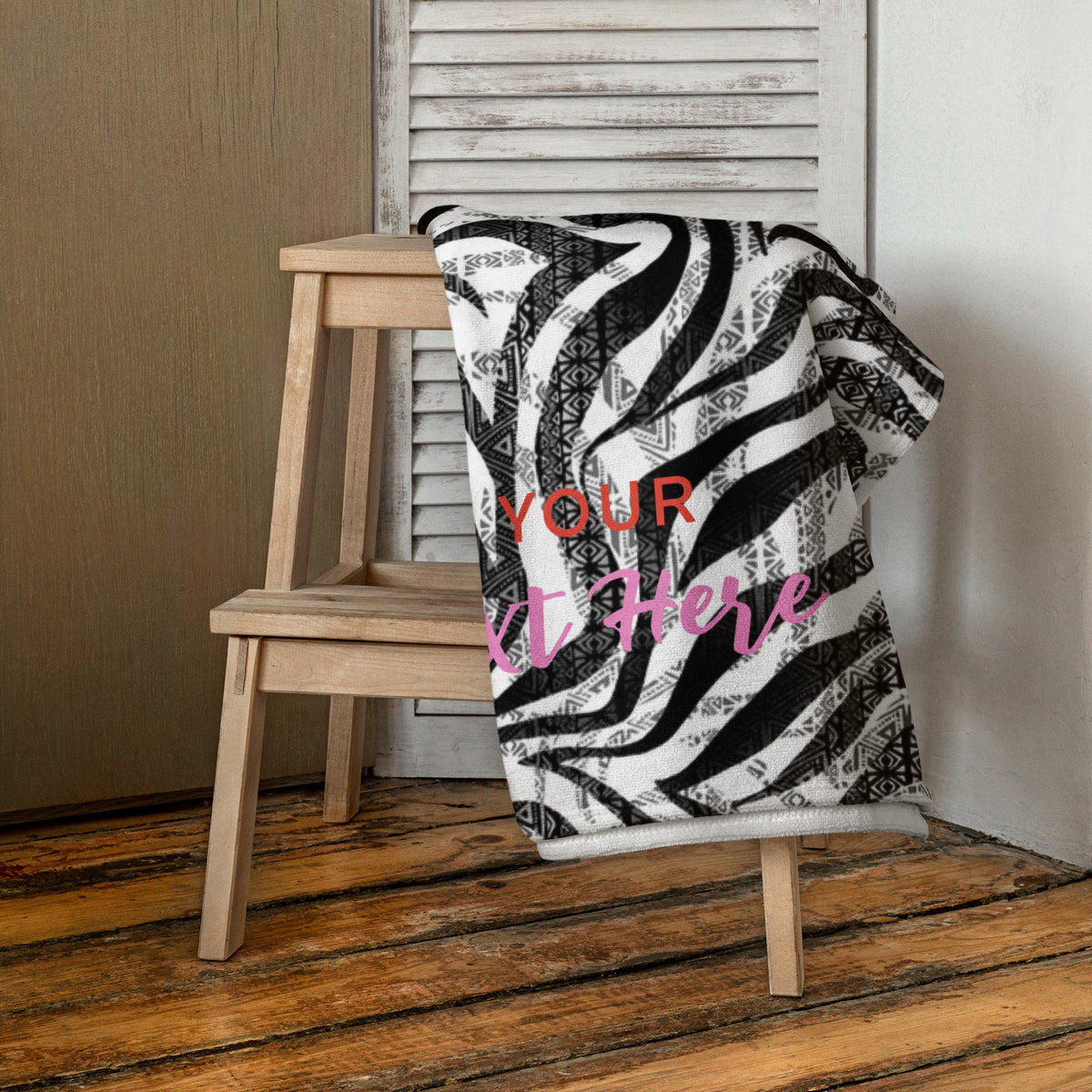 Personalisiertes Handtuch von CREWILD mit schwarz-weißem Zebra- und Ethno-Muster auf einem Holzhocker.