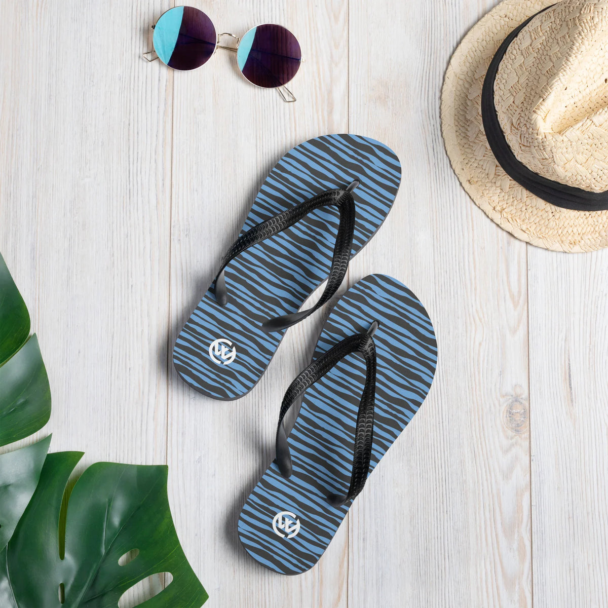 Blau-schwarze CREWILD Flip-Flops mit Wellenmuster auf hellem Holzhintergrund mit Sonnenbrille und Hut.