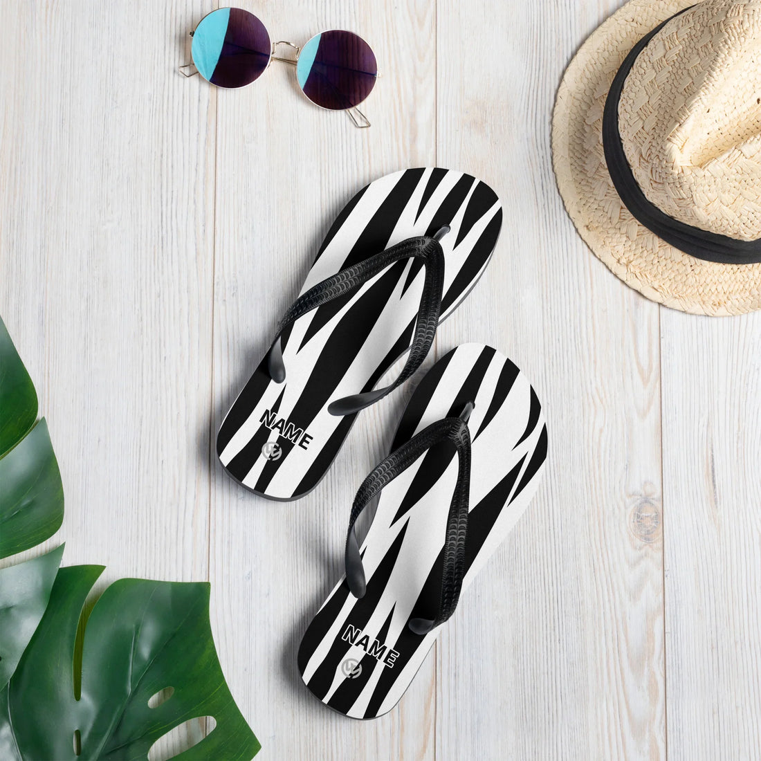 Personalisierbare CREWILD Flip-Flops mit schwarz-weißem Jungle-Muster auf hellem Holzhintergrund.