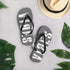 Graue CREWILD Flip-Flops mit weißem VIBES-Schriftzug neben einem Strohhut und grünen Blättern.