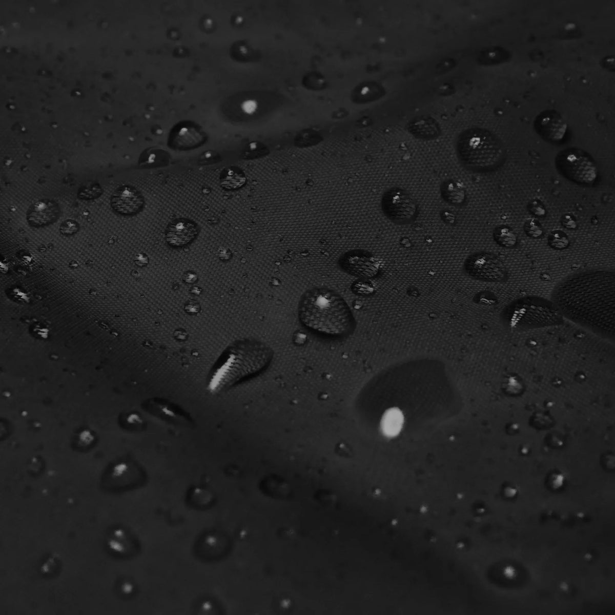 Detailansicht des wasserabweisenden, schwarzen Stoffes einer CREWILD Windjacke mit Wassertropfen