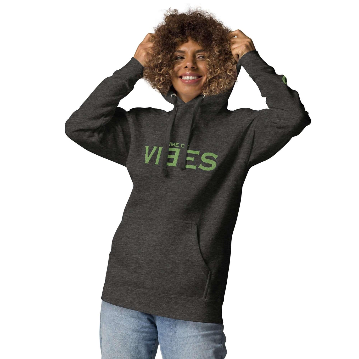 Frau trägt Unisex Premium Hoodie in Anthrazit mit grünem VIBES Print, lächelt, weiße Wand