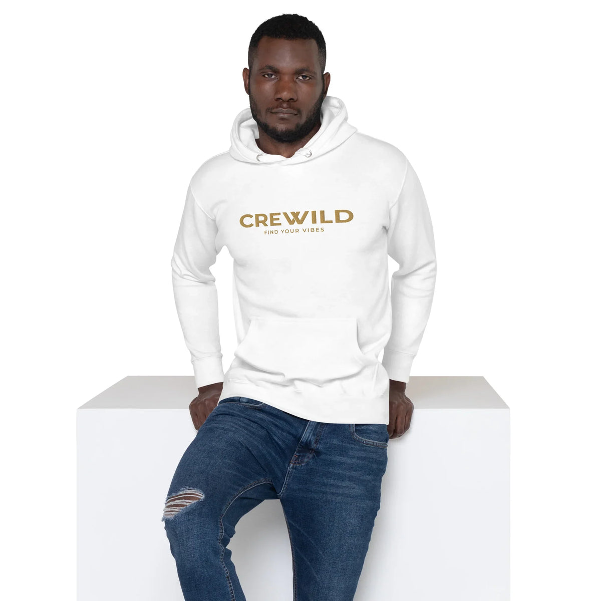 Mann in weißem CREWILD Hoodie und blauen Jeans lehnt an weißem Block