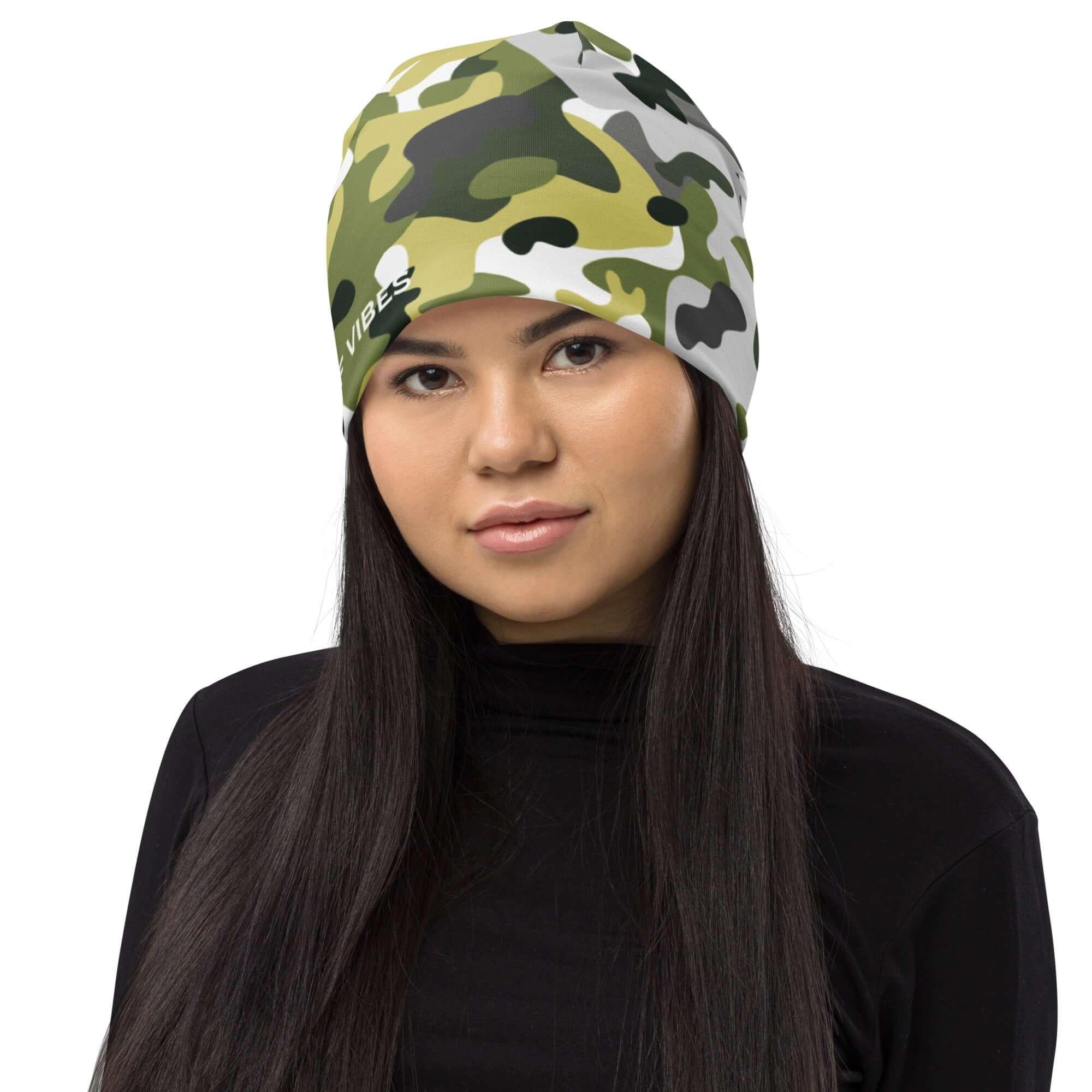 Frau mit langer dunkler Haar trägt Beanie mit Camouflage-Muster und VIBES-Logo vor weißem Hintergrund