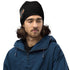 Mann mit schwarzer Beanie mit Flammen-Design und Schriftzug, blauer Jacke, weißer Hintergrund