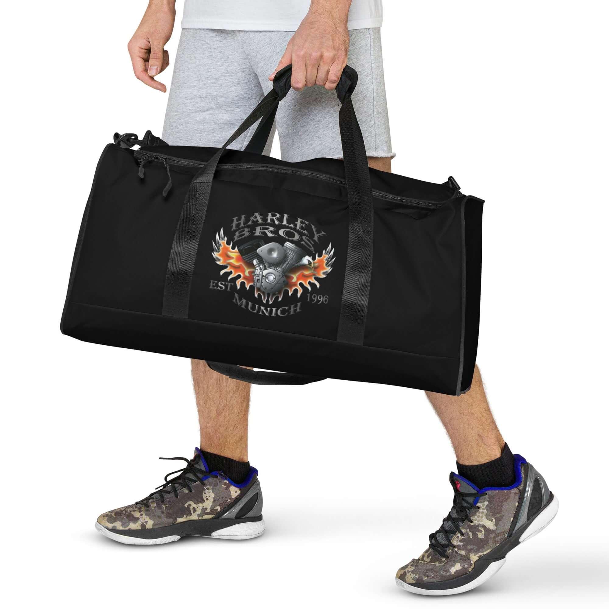 Schwarze Sporttasche mit Harley Bros München Logo und Flammenmuster, Mann trägt sie