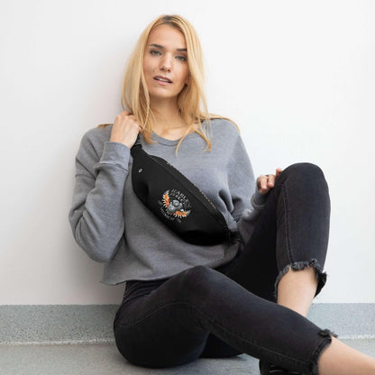 Frau mit grauem Sweatshirt und schwarzer Bauchtasche mit Harley-Motiv sitzt an Wand