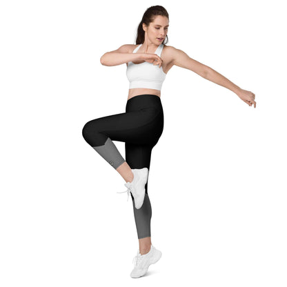 Frau in weißem Sport-BH und schwarz-grauen Leggings mit Taschen posiert vor weißem Hintergrund