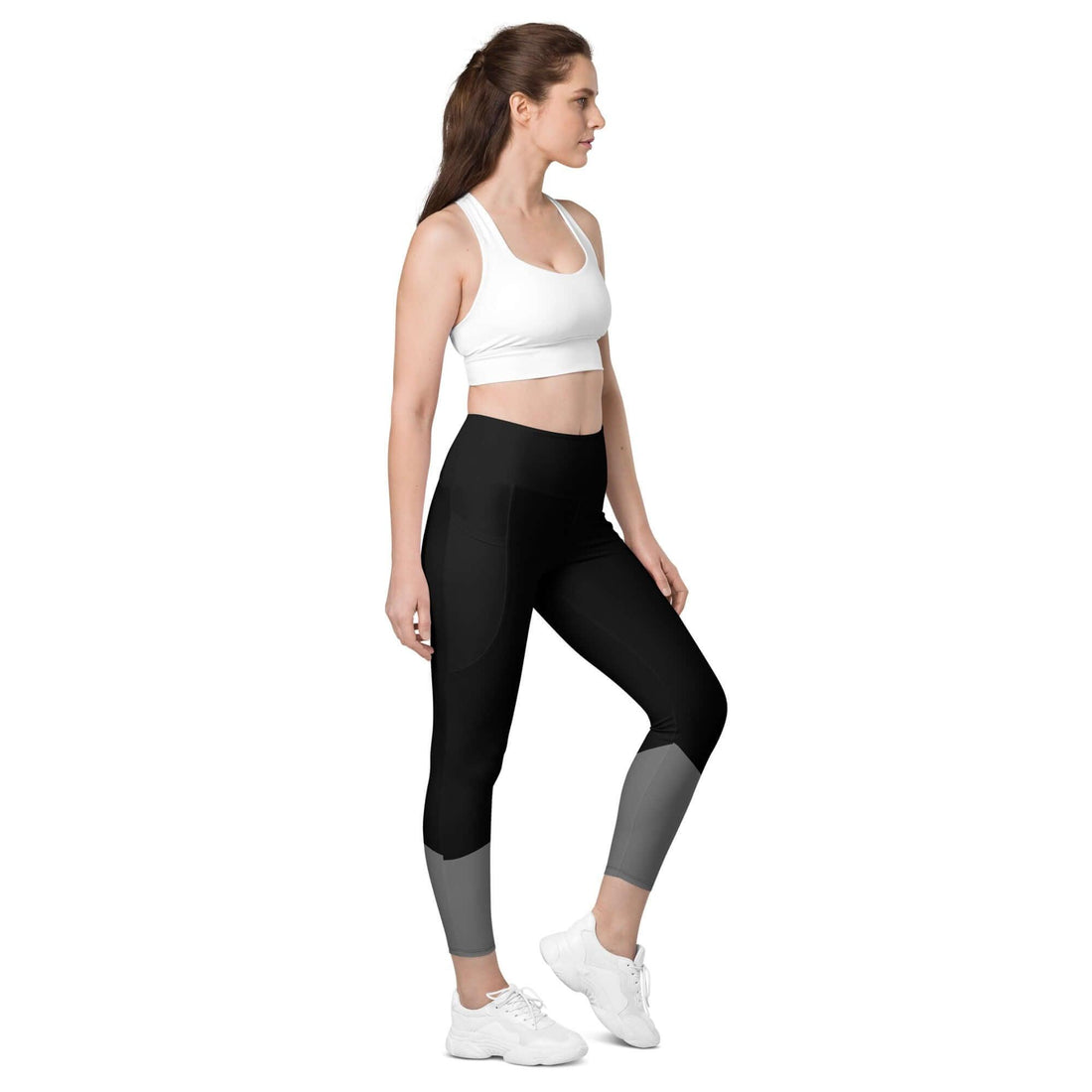 Frau trägt schwarze Leggings mit Taschen und grauen Details, weißer Sport-BH, Studio-Hintergrund