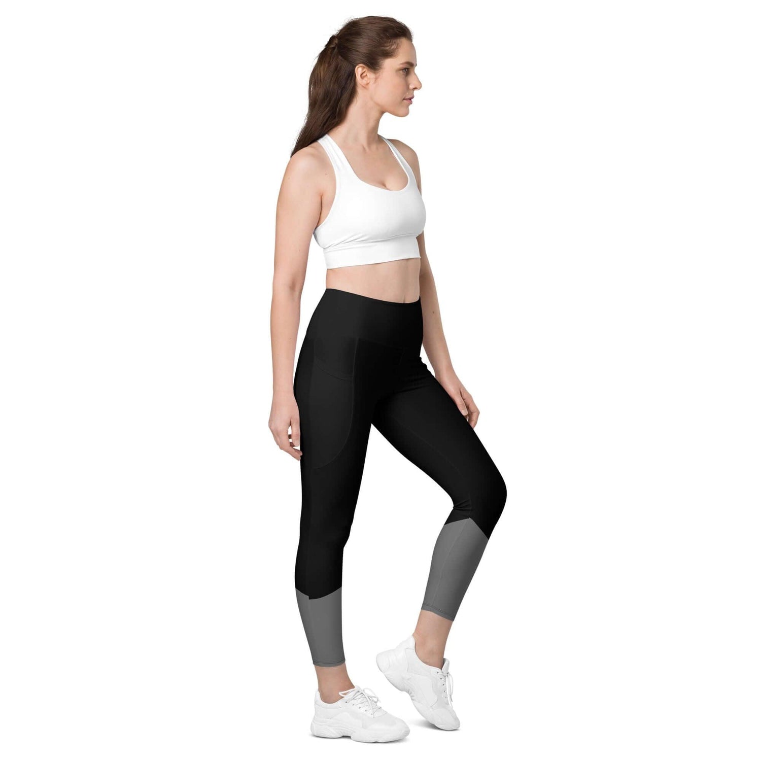 Frau trägt schwarze Leggings mit Taschen und grauen Details, weißer Sport-BH, Studio-Hintergrund