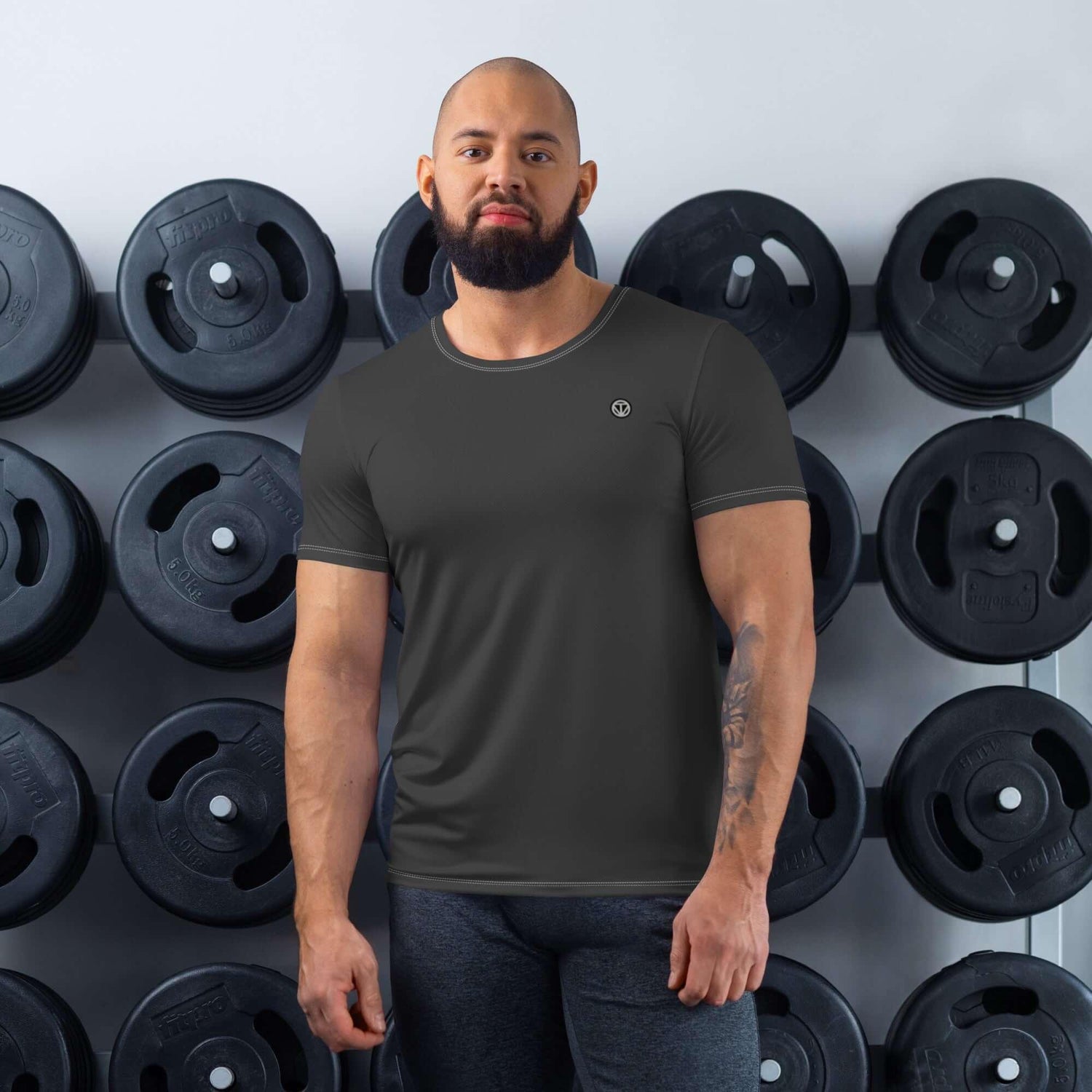 Mann im schwarzen Sport-Shirt steht vor Hantelgewicht-Wand im Fitnessstudio
