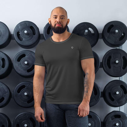 Mann im schwarzen Sport-Shirt steht vor Hantelgewicht-Wand im Fitnessstudio