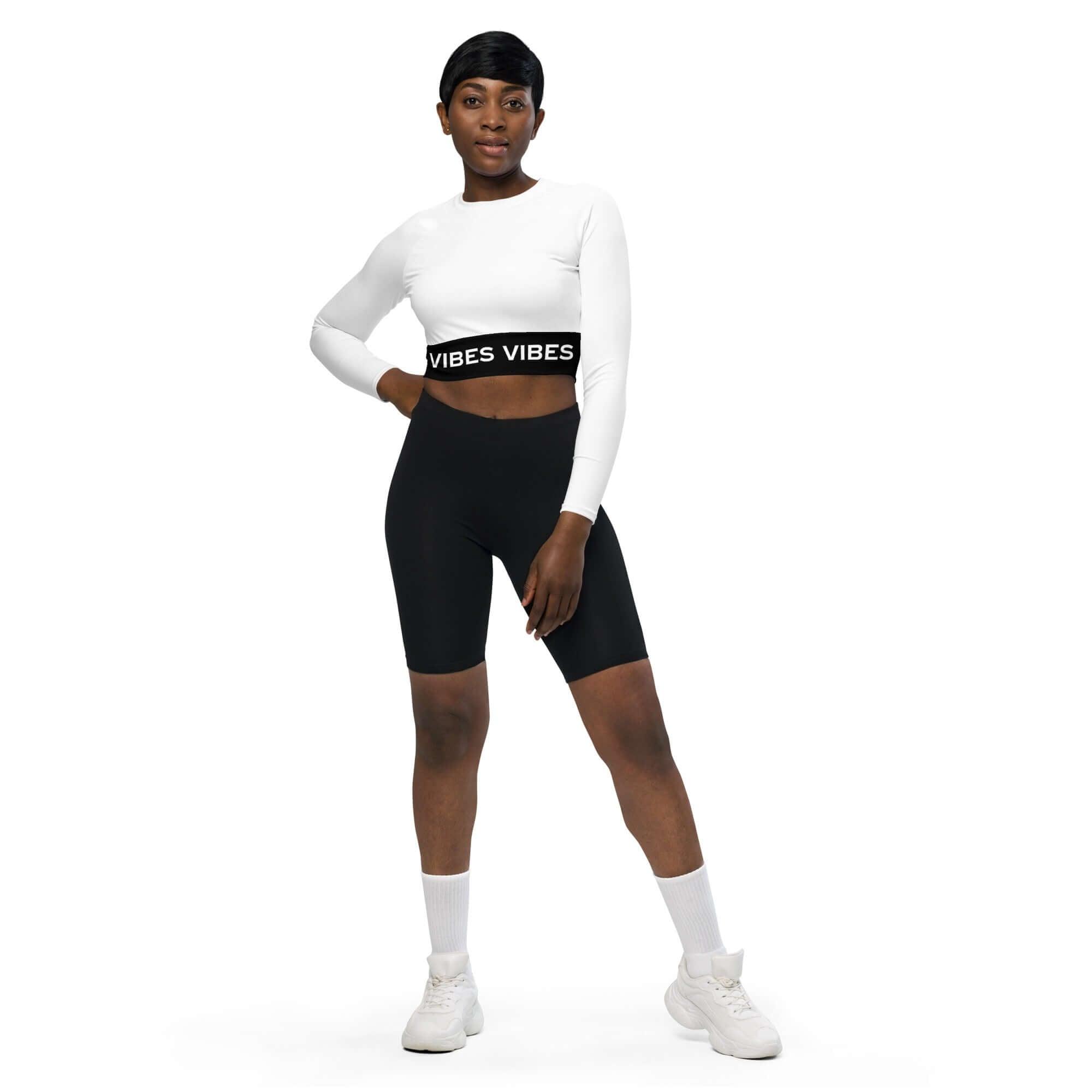 Frau trägt weißes Crop Top mit schwarzen Vibes-Bund und schwarze Radlerhose vor weißem Hintergrund