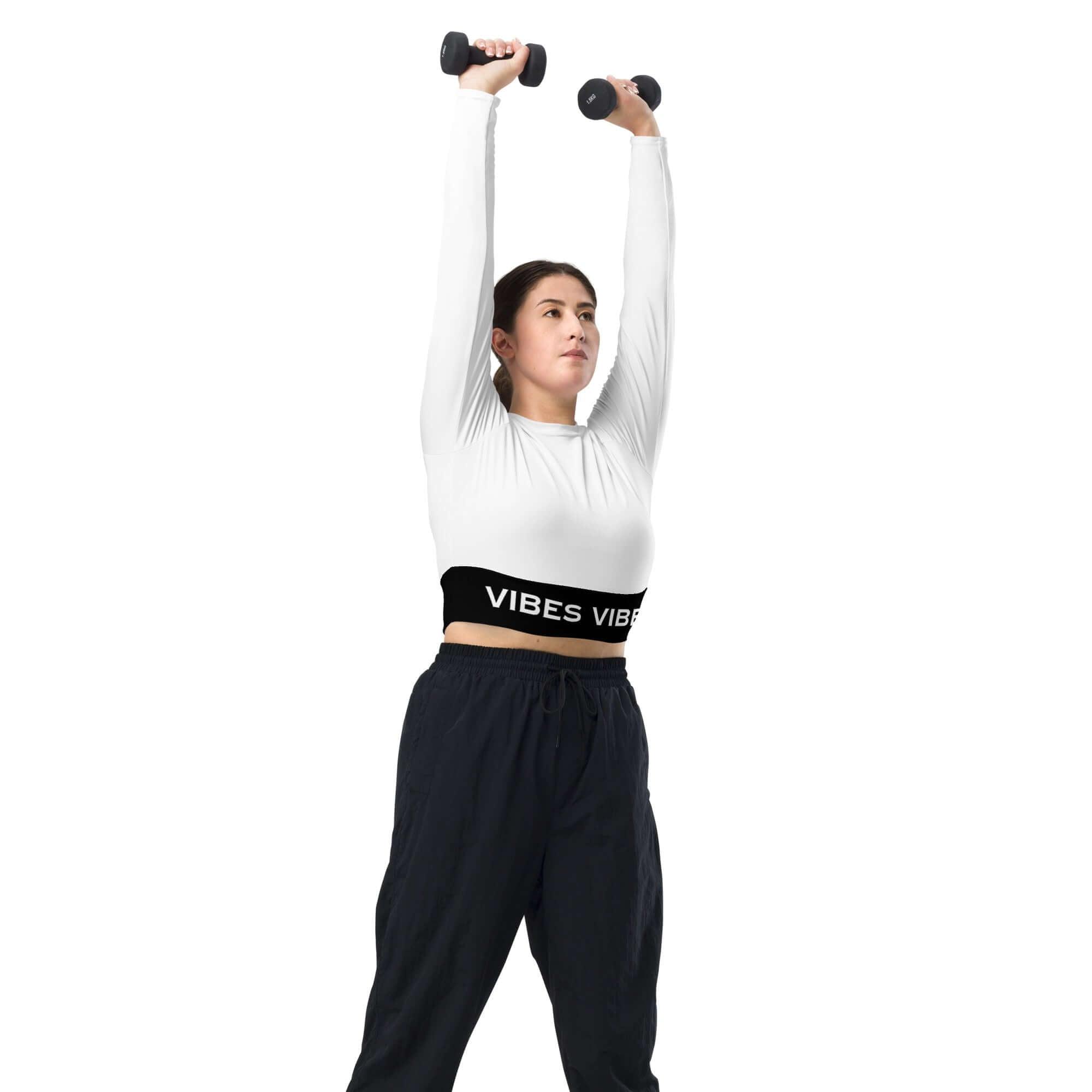 Frau im weißen Crop Top mit VIBES-Logo und Hanteln beim Training vor weißem Hintergrund