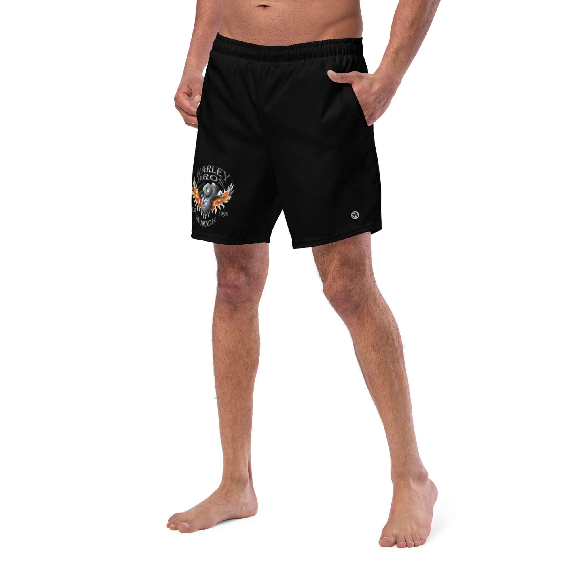 Mann trägt schwarze Badeshorts mit Harley-Motorrad-Print, weißer Hintergrund.