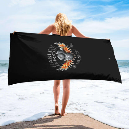 Frau hält schwarz bedrucktes Strandtuch mit Harley Bros Motiv am Meer