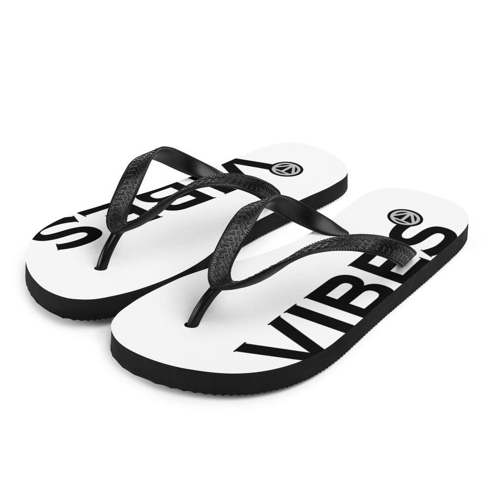 Weiße Flip Flops mit schwarzem VIBES Print und schwarzen Riemen auf weißem Hintergrund