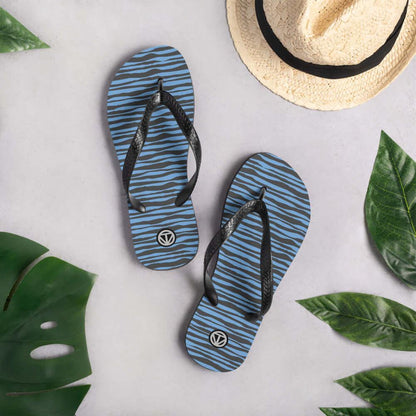 Blaue Flip Flops mit Zebramuster, Strohhut und grünen Blättern auf hellem Hintergrund