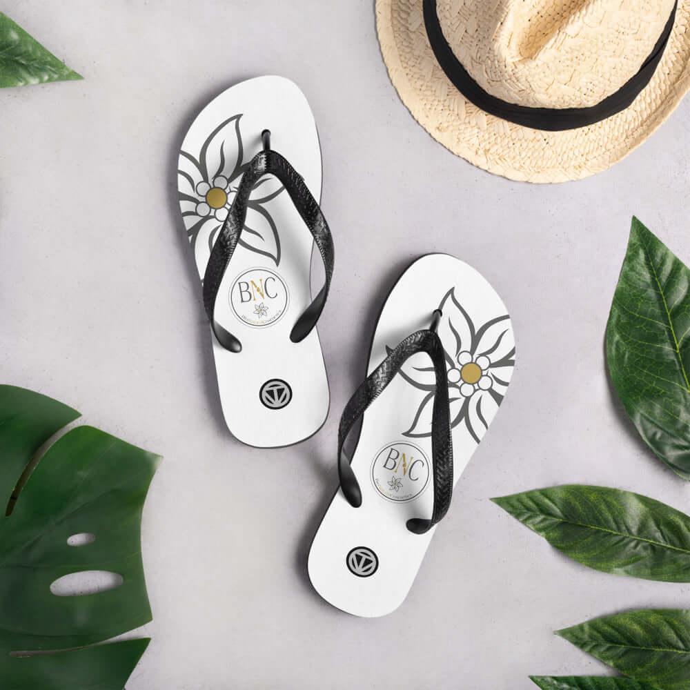 Weiße Flip Flops mit Blumenmuster und schwarzen Riemen auf grauem Hintergrund, Strohhut und Blätter